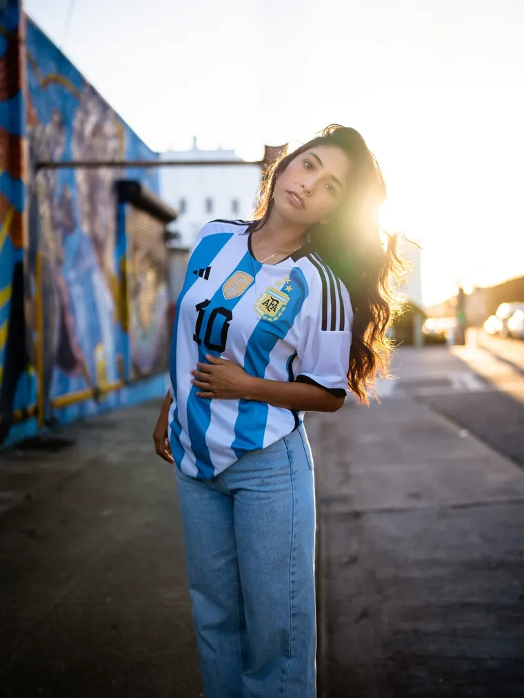 Woman in an Argentina shirt against a mural wall at sunset